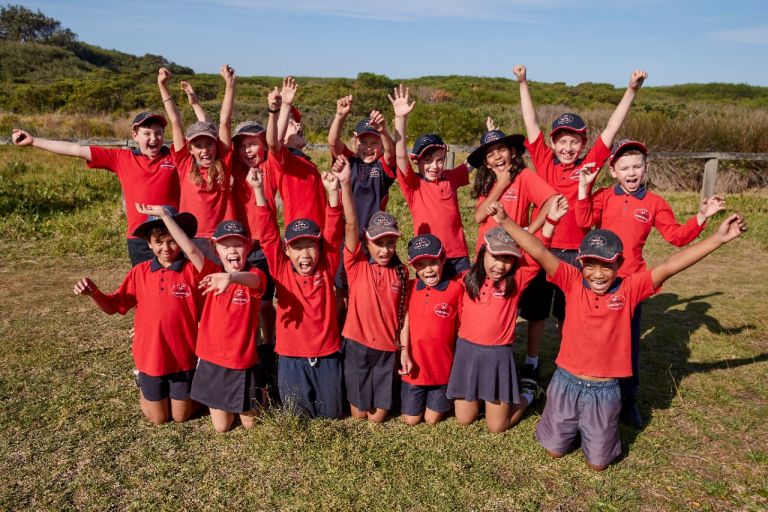 Large group photo of primary students near beach with hands up in the air 