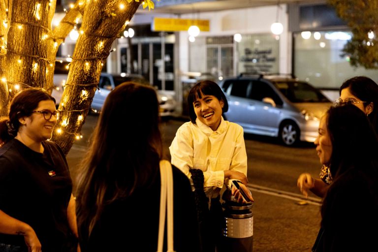 A group of women walking together on a city street lit up at night.