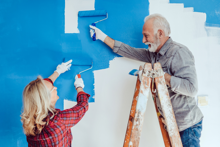 Two seniors painting a wall blue
