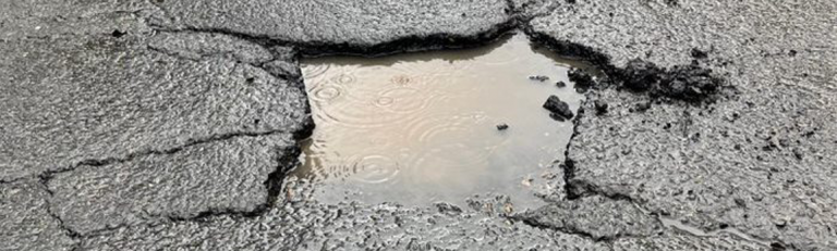 An image of a pothole in a road filled with a puddle.