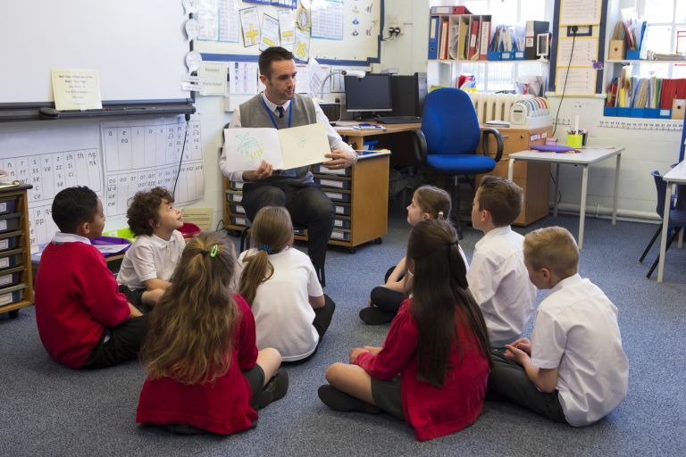 NESA teacher with book teaching a class of primary students in the classroom.