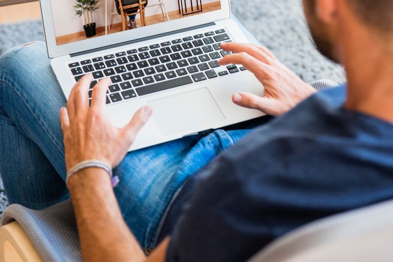 Closeup of a man wearing a navy top and blue jeans typing on a laptop