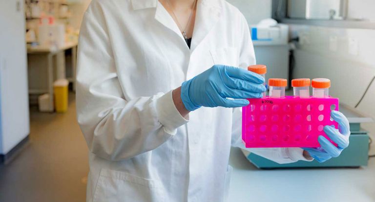 Sample carrying scientist in white lab coat with science equipment..