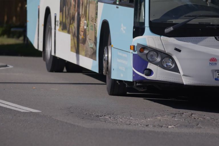 A bus is driving along a road, with a pot hole in front of it.