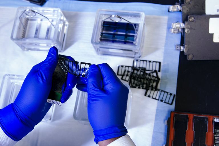Close-up of two gloved hands working on genome sequencing.