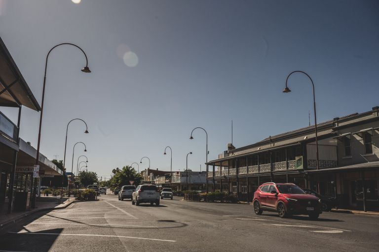 The main town strip of shops in Dubbo, with cars driving along the road and parked to the side.