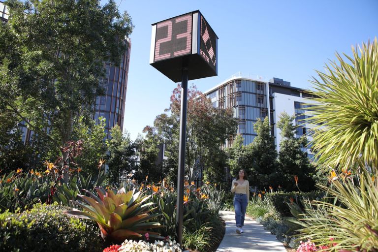 A woman walks along a pathway outdoors, looking up at a smart connected sign.