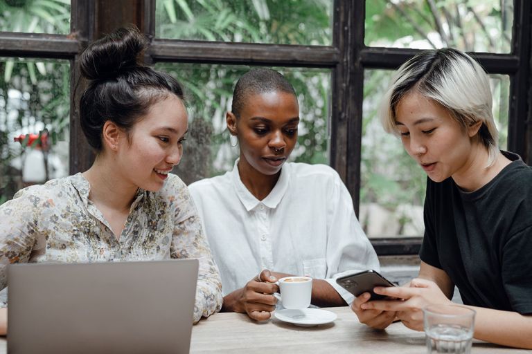 Three friends sit around a table drinking coffee and looking at a mobile phone