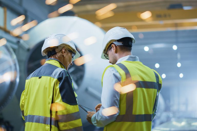 2 workers in hi-vis looking at a tablet inside a production facility