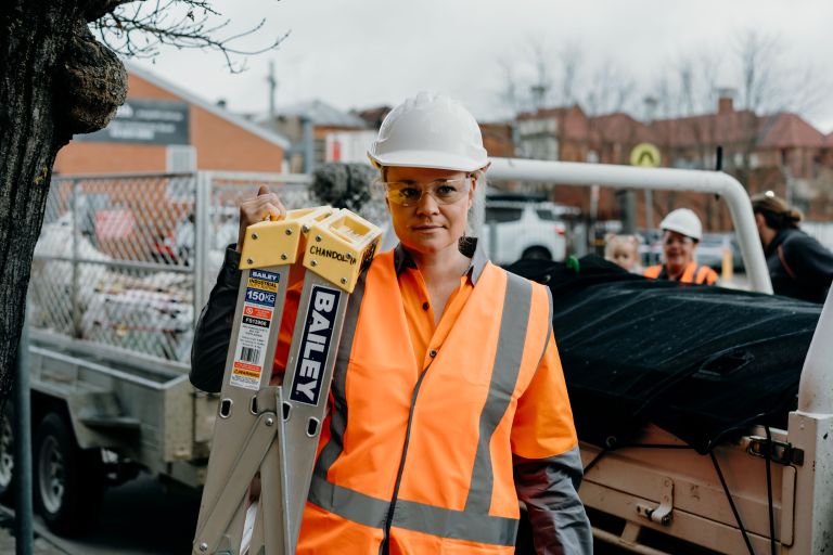 Annie on site in a hard hat carrying a ladder.