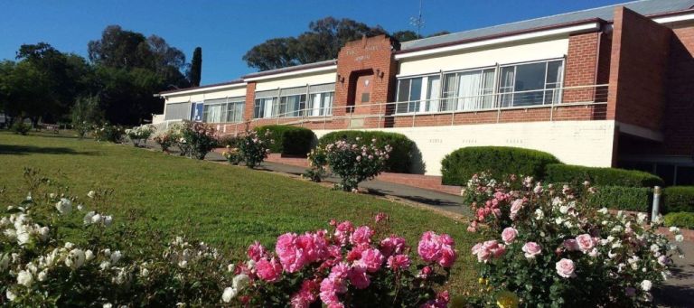 Main entry to the Yass District Hospital. Pink and white rose bushes line the driveway leading to the main entrance, which includes a wheelchair accessible entrance via a ramp. 