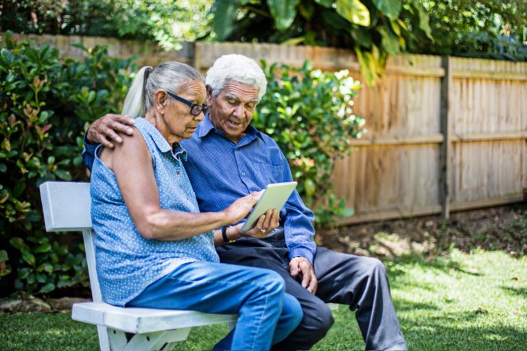 Two seniors looking at a tablet while sitting on a bench.