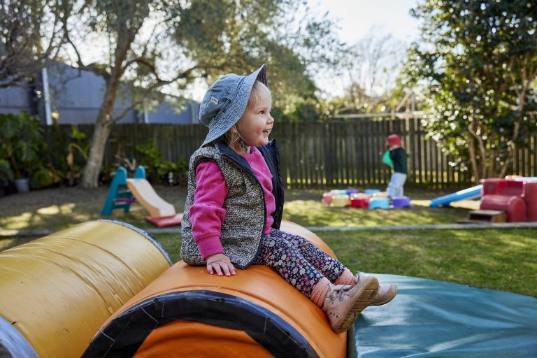 A smiling toddler sits on play equipment.