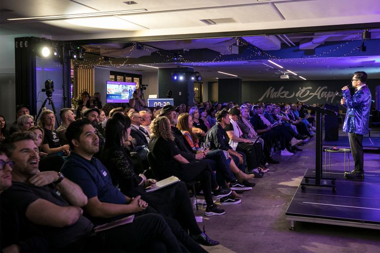 Crowd sitting in a room watching a man speak on the stage