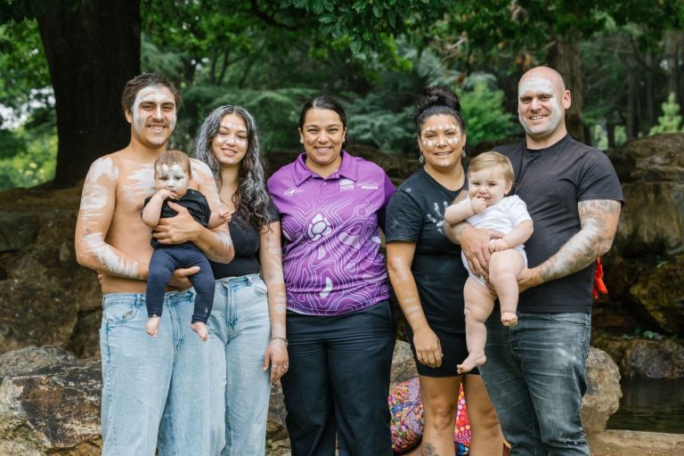 Aboriginal community members stand together outdoors with an Aboriginal health worker. They are facing forward and smiling.