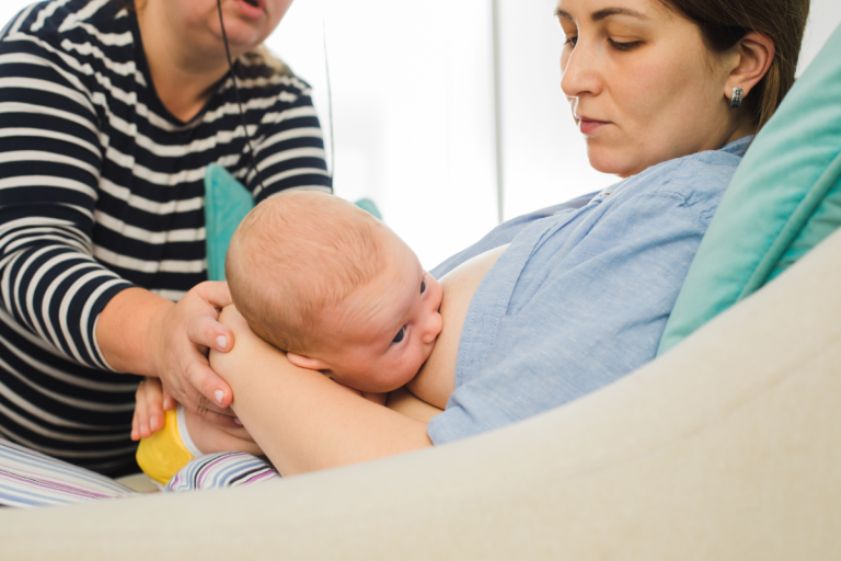 Photo of a mother breastfeeding a newborn, with assistance from a healthcare worker