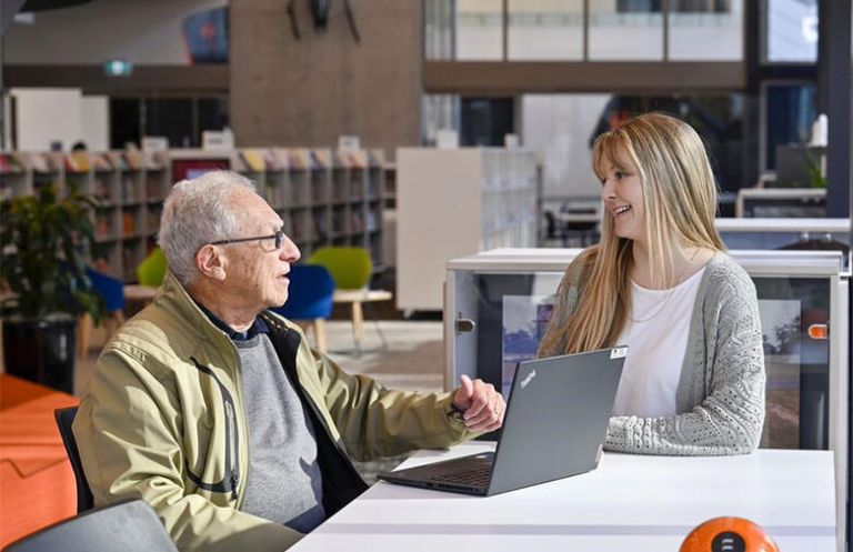 Two people sitting at a desk look at a laptop in Oran Park Library.