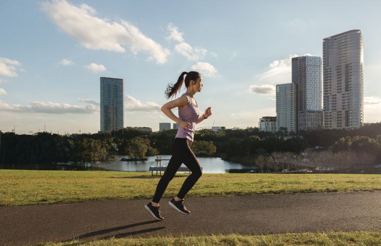 A person jogging on a footpath against a city backdrop.