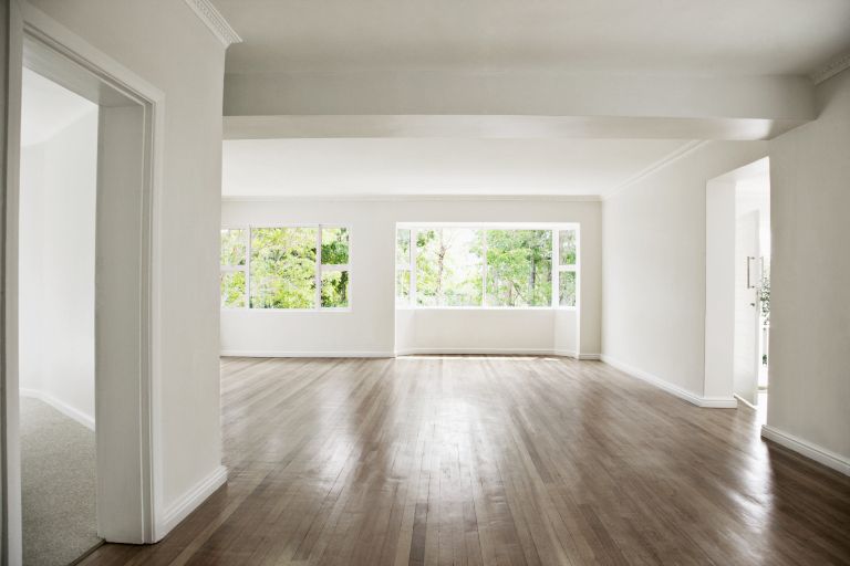Empty room with polished wooden floors reflecting sunlight coming through windows at rear.