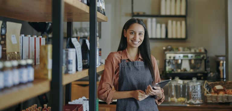 A barista stands in front of her coffee machine, smiling.