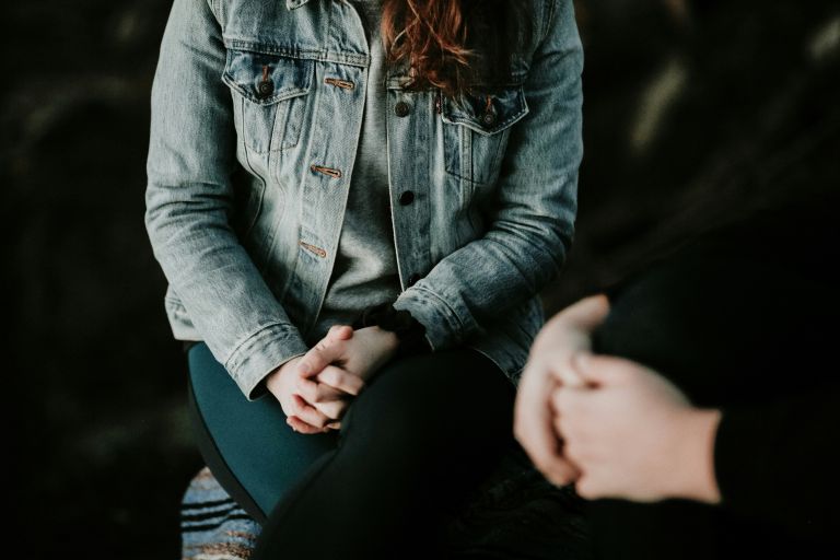 Two people with their hands clasped in their laps, talking.