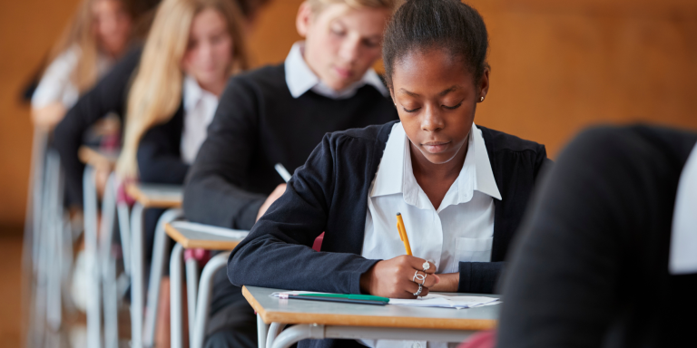 Students writing in an exam room, rows of desks