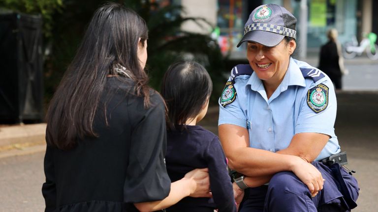 a police officer kneeling down smiling at a mother and child on the street