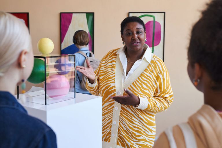 An art gallery tour guide speaks to a group of students about a colourful, modern sculpture.