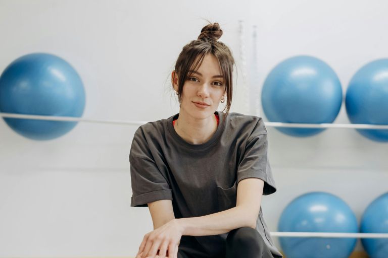 A young woman in a gym with fitness balls in the background.