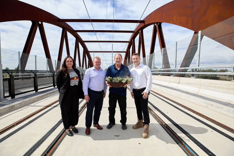 Four people stand in the centre of a steel arch bridge