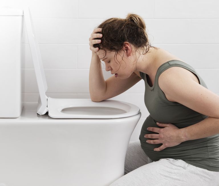 Pregnancy women feeling nauseous, leaning over a toilet