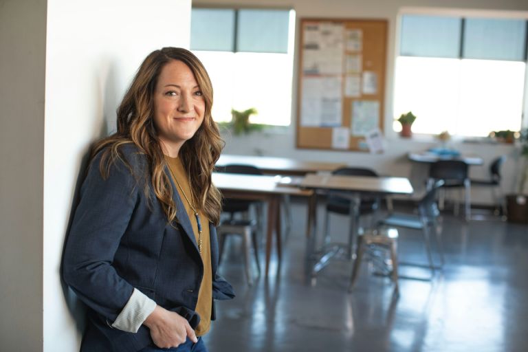 Teacher leaning against the wall in an empty classroom.