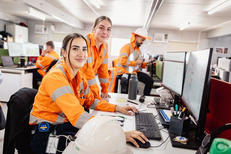 Two female workers in bright orange protective clothing sitting by a computer