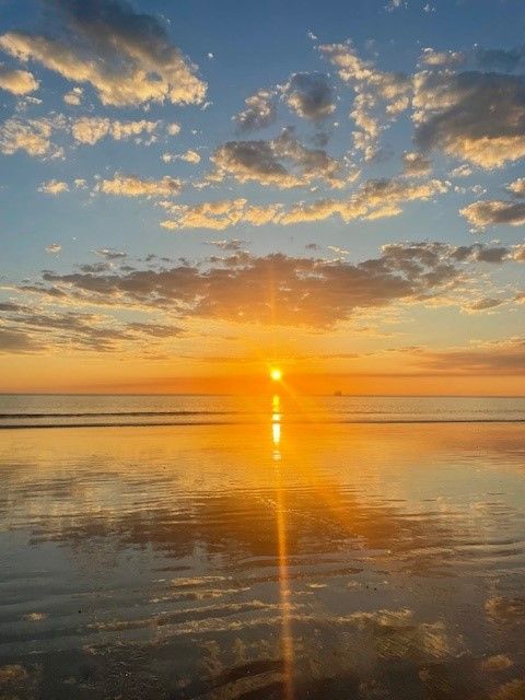 Blue sky with some clouds, setting sun, ocean and sand