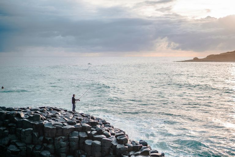  Man on rocky shore, looking out at the ocean, fishing.