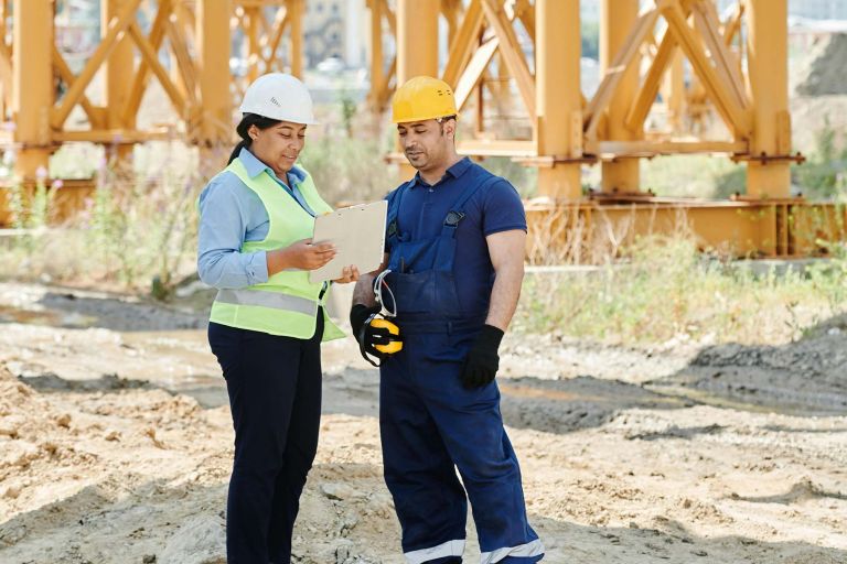 Two female and male workers standing having a conversation at an outdoor worksite. 