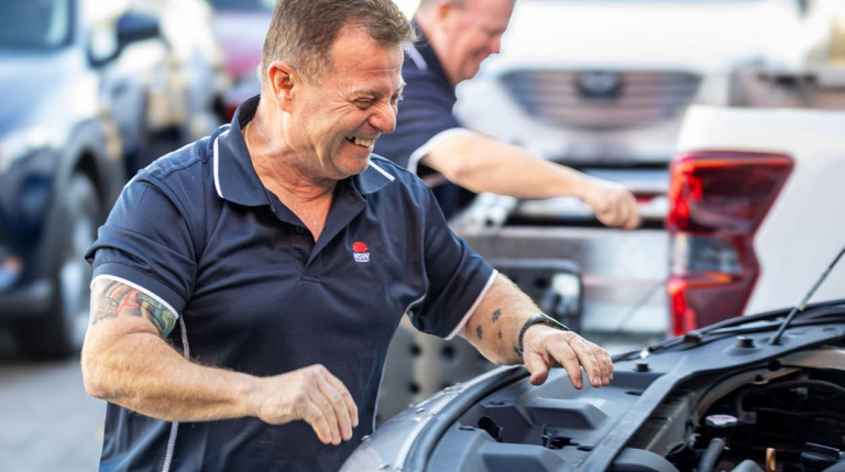 A smiling man wearing a NSW Government shirt working on a car.