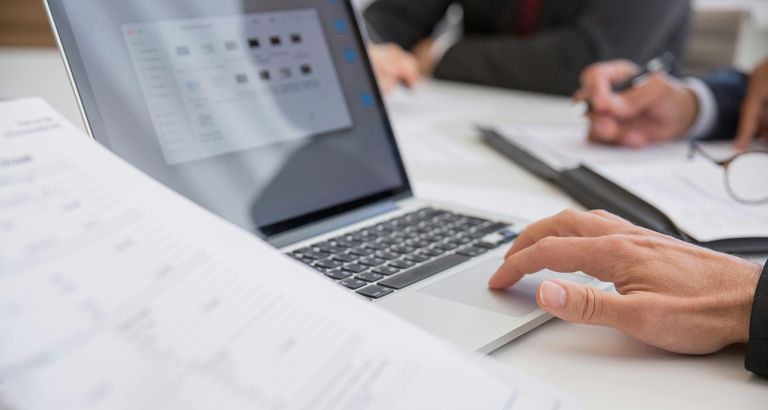 Person working on laptop with documents on desk.