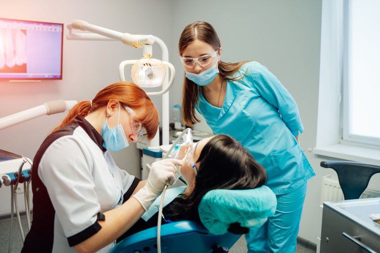 Dentist and a nurse in masks and protective glasses treating patient's teeth.