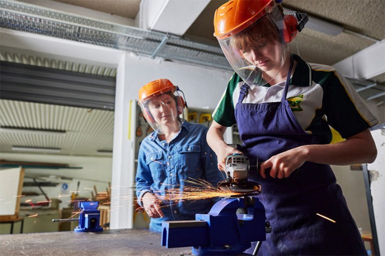 Female apprentice being supervised while using grinder