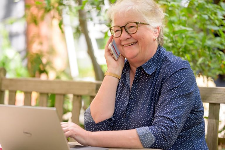 A lady on the phone sitting in front of a laptop.