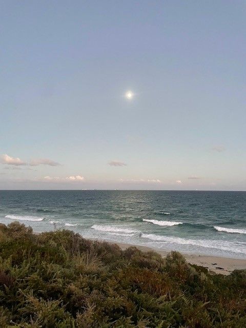 Early morning blue sky with some clouds, the moon, ocean and sand