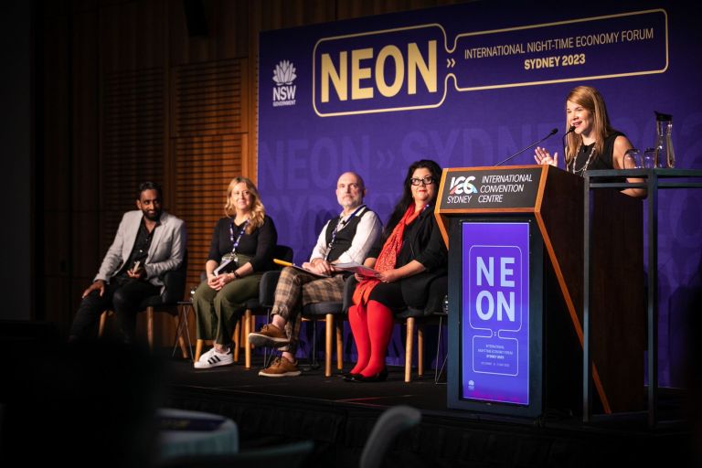 Person speaking on stage with panelists at NEON Forum event 