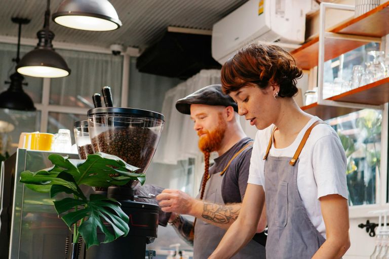 A female and a male hospitality workers making coffee.