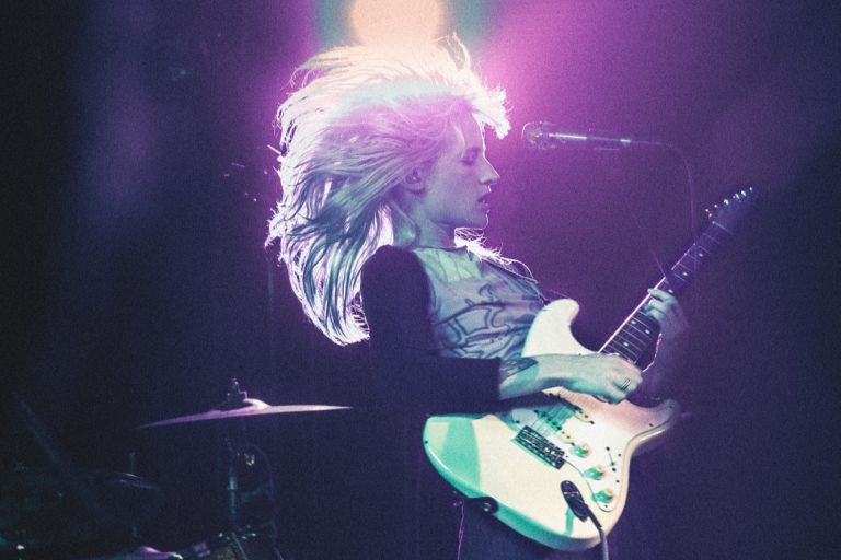 Zoe Catterall of The Buoys playing guitar on stage with hair blown back