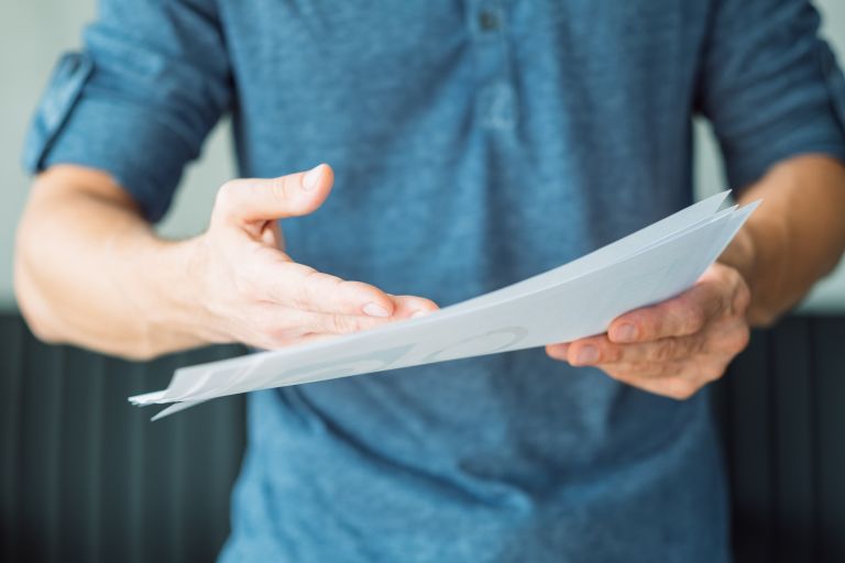 Man in a blue shirt holding a piece of paper pointing at it.