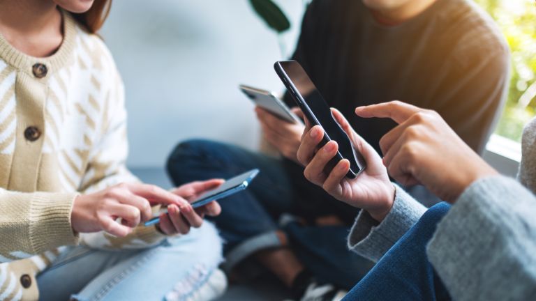 Three people gathered in a circle on their mobile devices.