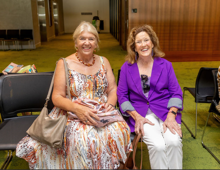 Two ladies sitting side by side smiling