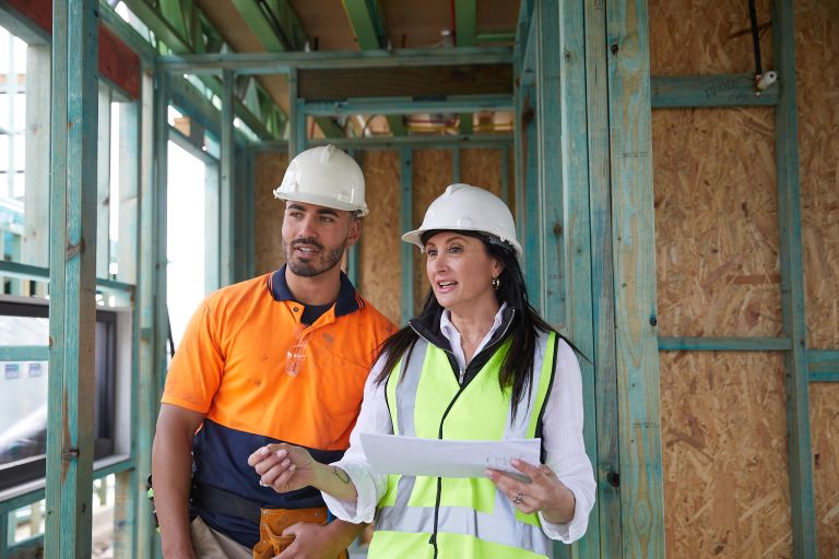 Construction worker and supervisor in safety gear discussing plans at a building site