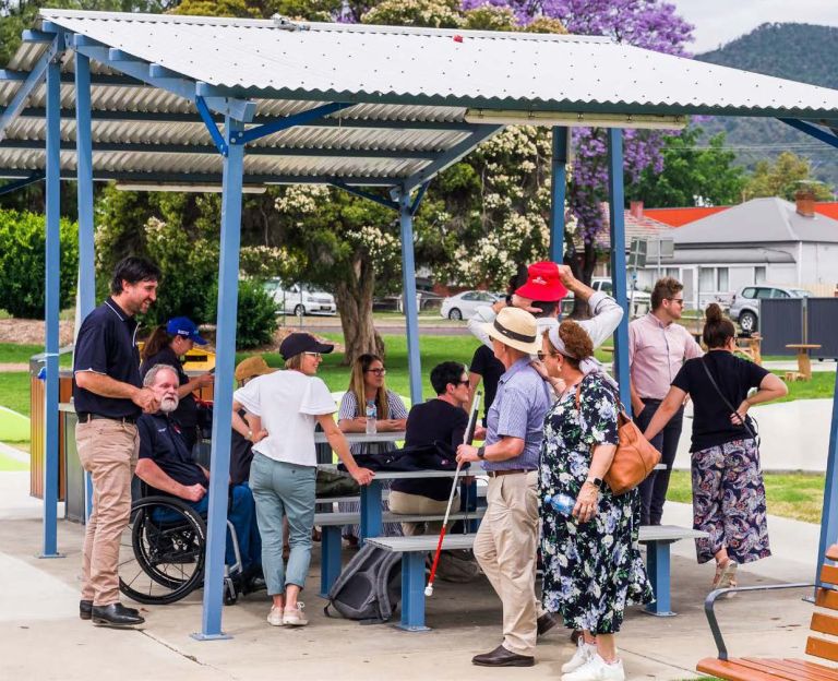 A group of people with diverse abilities gathering around tables at an accessible playground for International Day of People with Disability